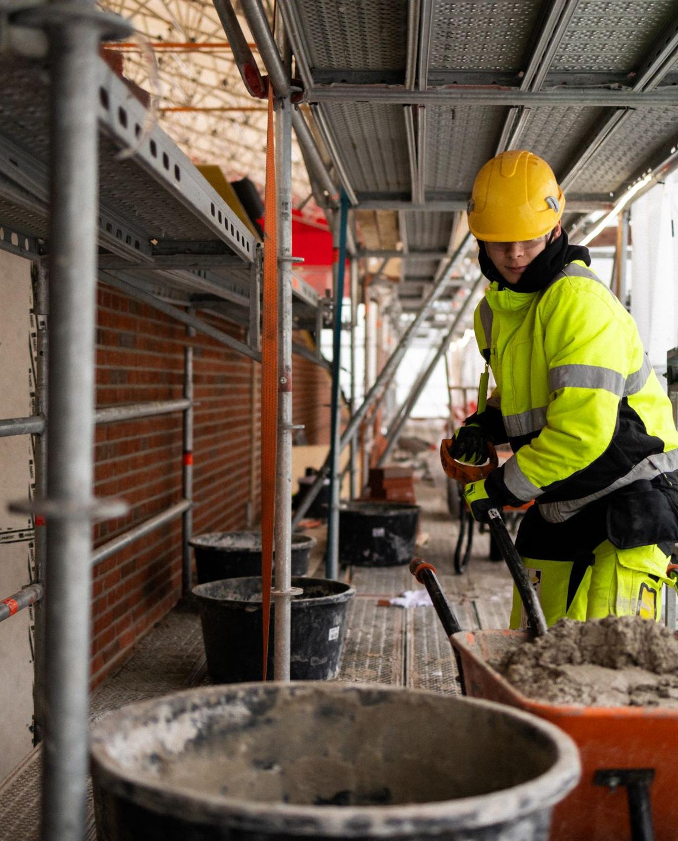 Korjausrakennuksen ammattilainen lapioimassa ty&ouml;maalla sementti&auml;.