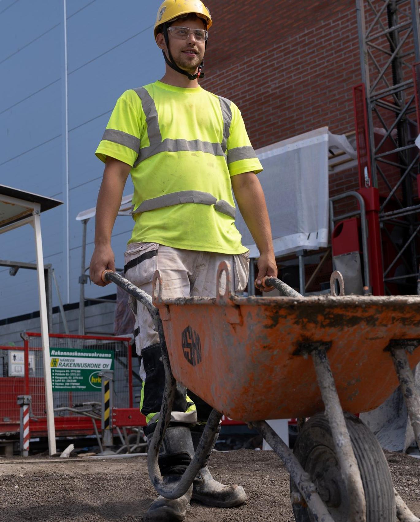 Nurmijärven muurareiden muurari työntämässä kottikärryä rakennusmaalla.